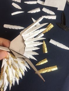 someone is cutting out some white and gold paper feathers with scissors on the table next to them