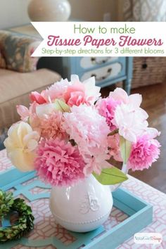 a white vase filled with pink and yellow flowers on top of a blue tablecloth