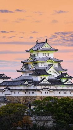 a tall white building sitting on top of a lush green hillside under a pink sky