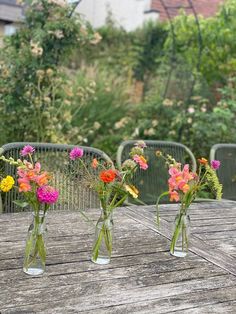 three vases filled with colorful flowers sitting on top of a wooden table in front of a garden