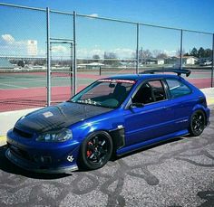 a blue car parked on the side of a tennis court next to a chain link fence