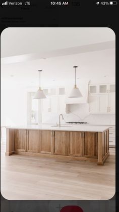 an empty kitchen with white cabinets and wooden flooring is pictured in this image, there are two pendant lights hanging over the island