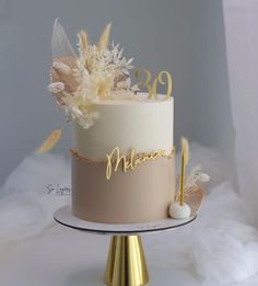 a white and gold wedding cake with feathers on top, decorated with the number 98