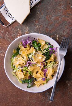 a white bowl filled with pasta and veggies on top of a brown table