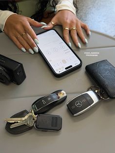 a woman holding a cell phone next to several keys and wallets on a table