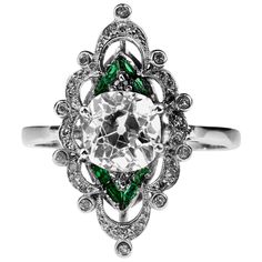 A vibrant Edwardian diamond and emerald ring, set in platinum. Its beautiful design consists of a central set old cushion cut diamond and trillions of emeralds which are surrounded by scrolls of diamonds. This ring is a fine example of Edwardian elegance and the jeweller's art - the intricate detailing and setting accentuate the beautiful color of the emeralds and brilliance of the diamonds. The level of intricacy and detail is unique. 1 x cushion cut diamond centre, approximate weight 2.0 carat Diamond And Emerald Ring, Edwardian Diamond Ring, Edwardian Engagement Ring, Edwardian Ring, Edwardian Jewelry, Platinum Diamond Engagement Rings, Cushion Cut Diamond, Platinum Diamond Rings, Modern Engagement Rings