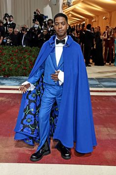 a man in a blue suit and cape standing on a red carpet