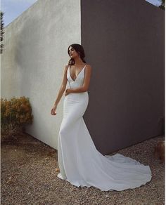 a woman standing in front of a wall wearing a white dress and posing for the camera