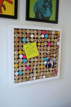 a cork bulletin board with pictures on the wall behind it and a note pinned to one of the corks