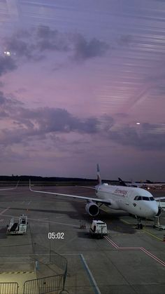 an airplane is parked on the tarmac at dusk with clouds in the sky behind it