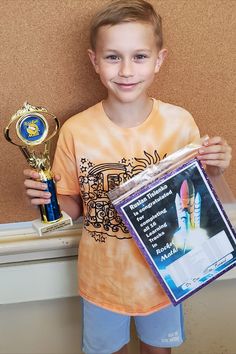 a young boy is holding two trophies and posing for the camera with his award plaque