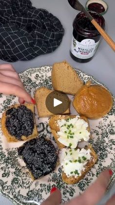 a plate with bread, jams and other food items on it next to a woman's hands