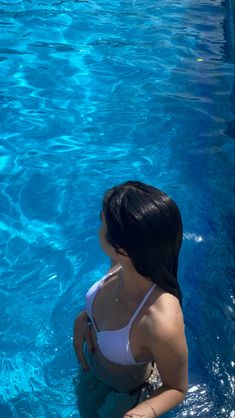 a woman in a white bathing suit sitting on the edge of a pool next to a dolphin