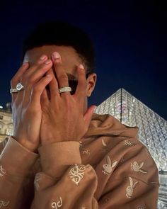 a man covers his face with his hands in front of the pyramids at night