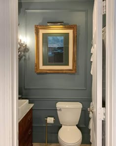 a white toilet sitting in a bathroom next to a sink under a framed painting on the wall