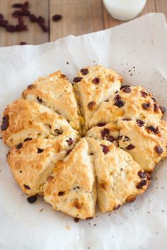 a pastry with raisins on top is cut in half and sits on a piece of parchment paper next to a glass of milk