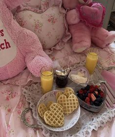 a pink teddy bear sitting on top of a bed next to waffles and fruit