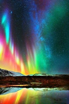 the aurora bore is visible in the night sky above mountains and water, with bright lights on