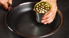 a person holding a can on top of a metal tray with holes in it and the lid open