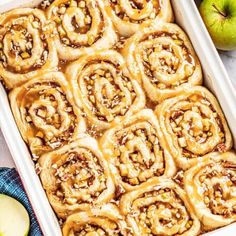 apple cinnamon rolls in a white baking dish with apples around the edges and on top