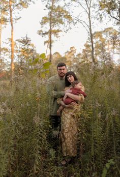 a man and woman standing in tall grass with trees in the backgrouds