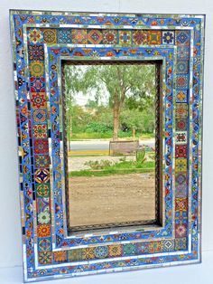 a colorful mirror with a bench in the middle and trees behind it, on a white wall