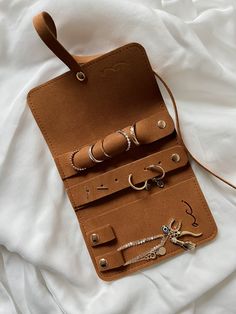 a leather case with rings and bracelets in it on a white bed sheet next to a pair of scissors