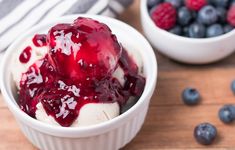 two bowls filled with ice cream and blueberries on top of a wooden table next to another bowl