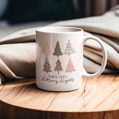 a white coffee mug sitting on top of a wooden table next to a pillow and blanket