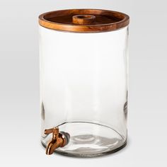 a glass jar with a wooden lid and handle on the bottom is holding a metal faucet