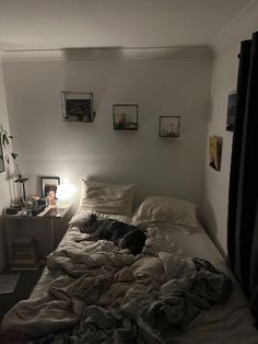 an unmade bed in a small room with pictures on the wall above it and a lamp next to it