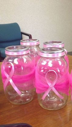 four jars with pink ribbons on them sitting on a table