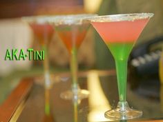 three martini glasses sitting on top of a table next to each other with green and pink liquid in them