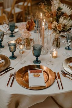 the table is set with gold plates and silverware, candles, and flower centerpieces