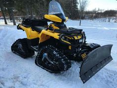 a yellow and black snowmobile parked in the snow with a plow attached to it