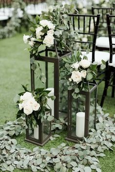 two lanterns with white flowers and greenery on the ground