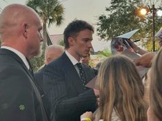 a man in a suit is signing autographs for people at an outdoor event with palm trees behind him