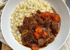 a white bowl filled with meat and carrots on top of mashed cauliflower