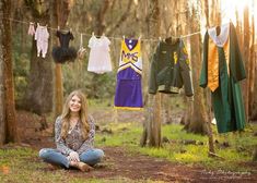 a woman sitting on the ground in front of clothes hanging from a line and trees