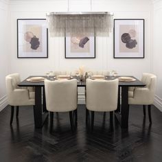 a dining room table with chairs and pictures on the wall above it, along with two chandeliers