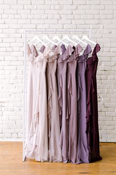 four dresses hanging on a rack in front of a white brick wall and wooden floor