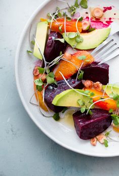 a white plate topped with beets, carrots and avocado next to a fork