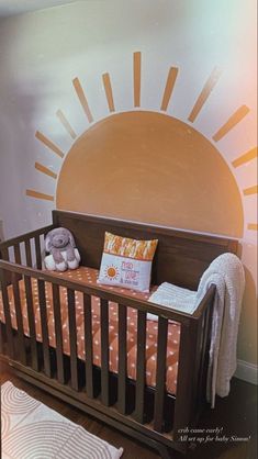 a baby's crib in front of a sun painted on the wall behind it