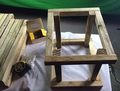 two wooden stools sitting on top of a white sheet covered table next to a green screen