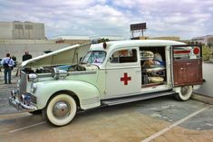 an old white ambulance parked in a parking lot with people standing around and looking at it