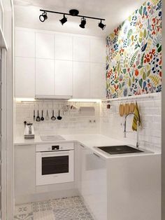 a kitchen with white cabinets and colorful wallpaper