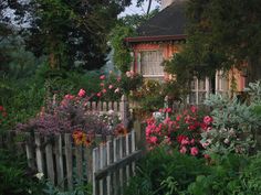 an old house with flowers in front of it and a picket fence around the yard