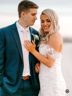 a bride and groom standing next to each other in front of the ocean at sunset