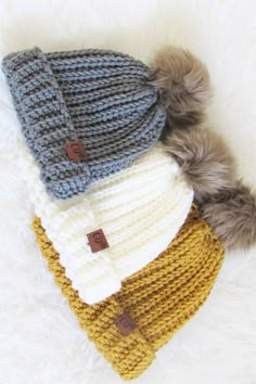 three knitted hats with pom - poms laying on top of each other