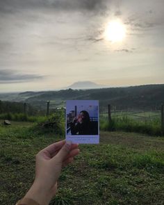 a person holding up a polaroid in front of a field with the sun behind them